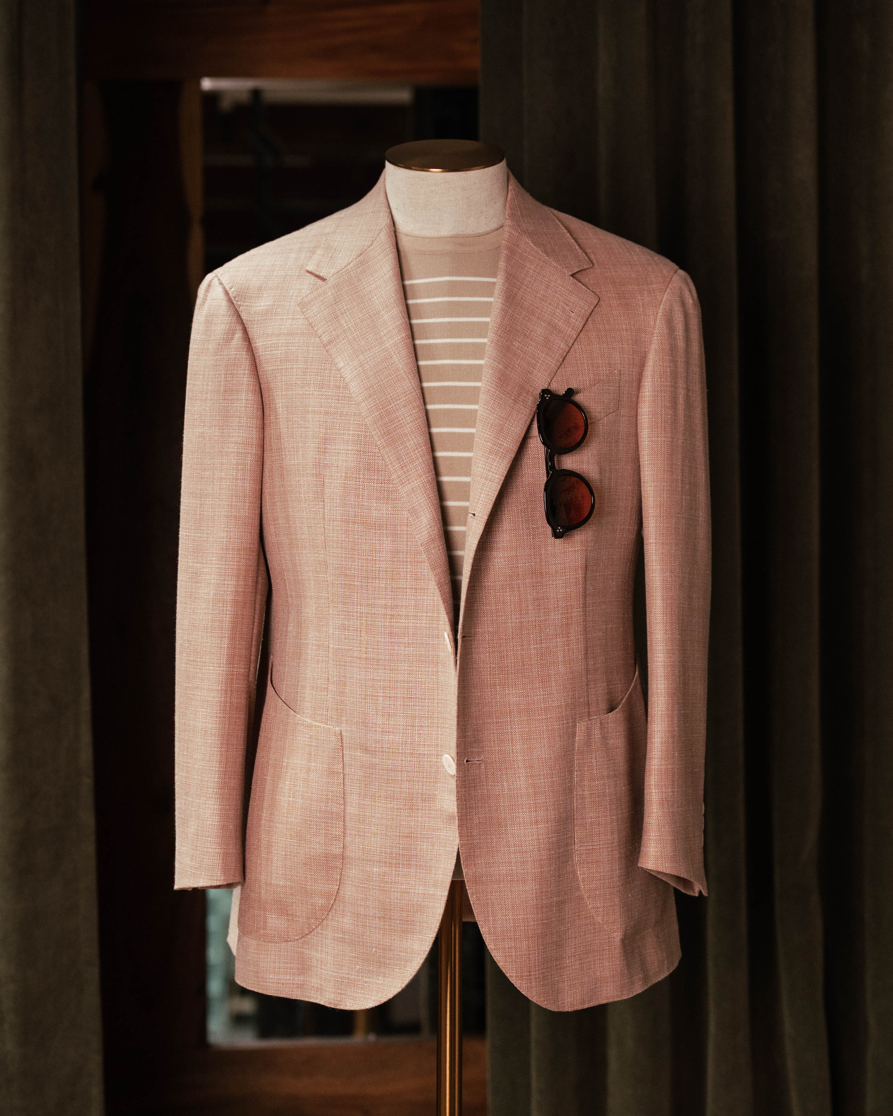 Pink blazer on a mannequin with sunglasses in the pocket against a dark background