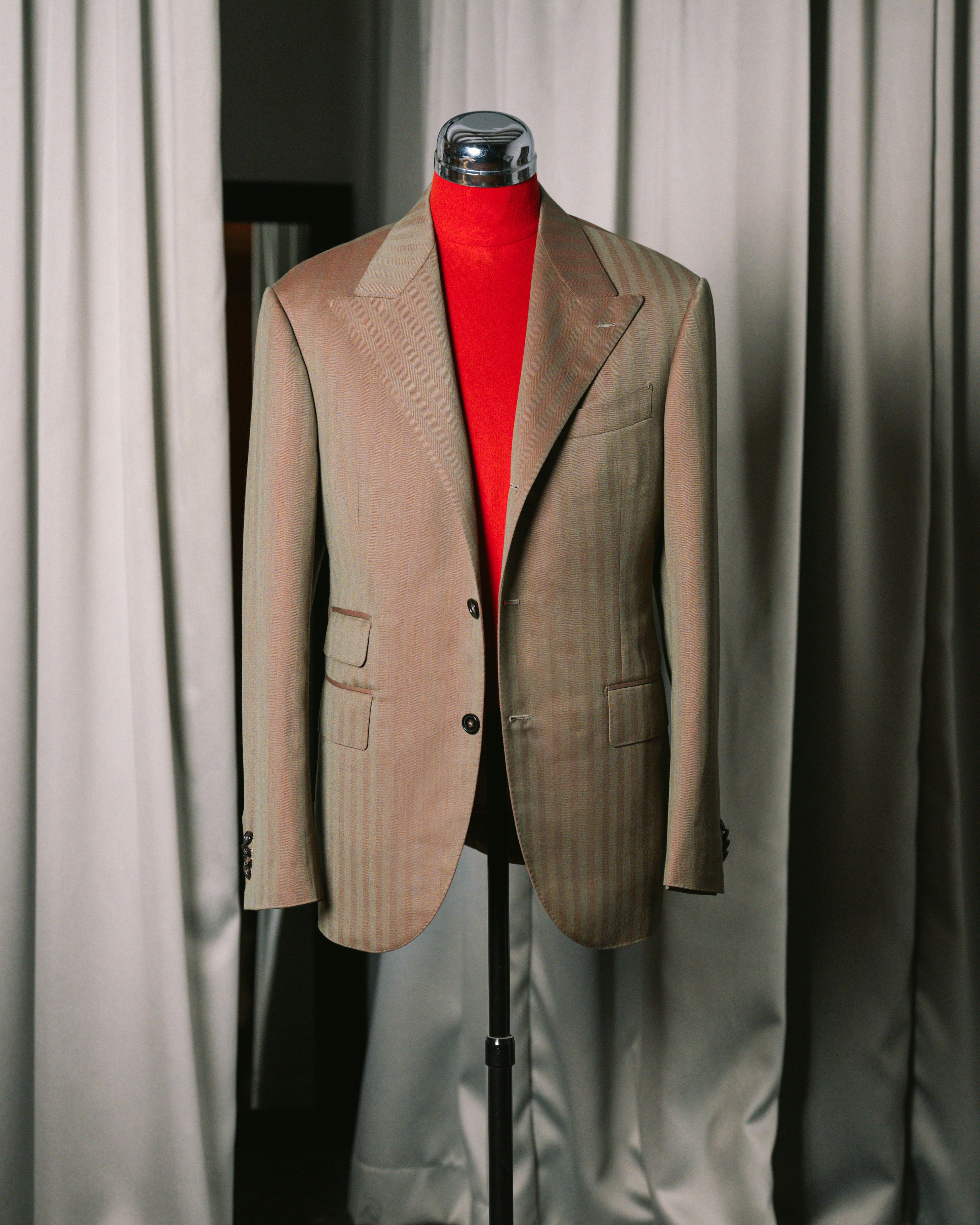 Khaki blazer on a mannequin with a red shirt against a neutral curtain background