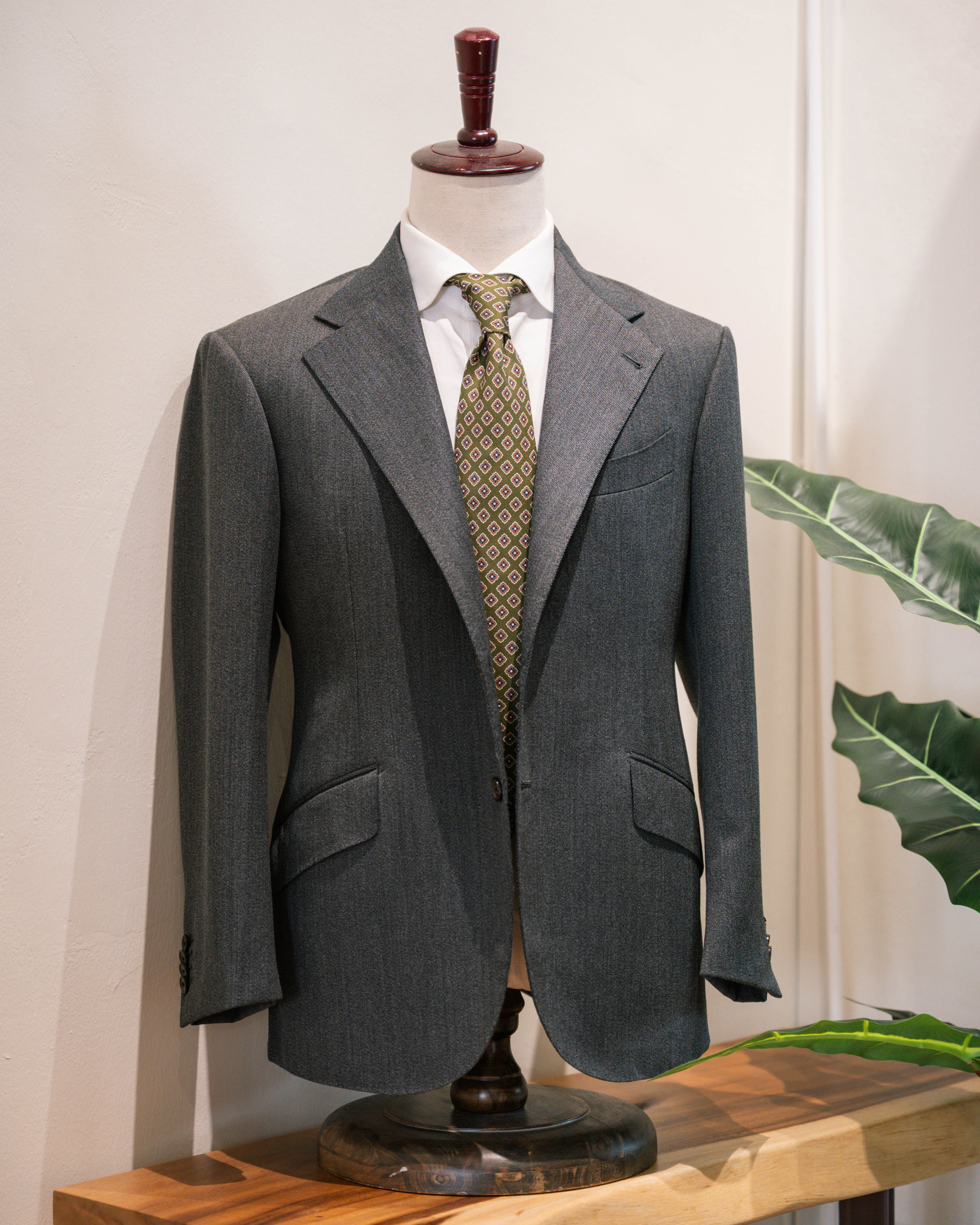 Gray suit jacket on a mannequin with a white shirt and patterned tie against a neutral background