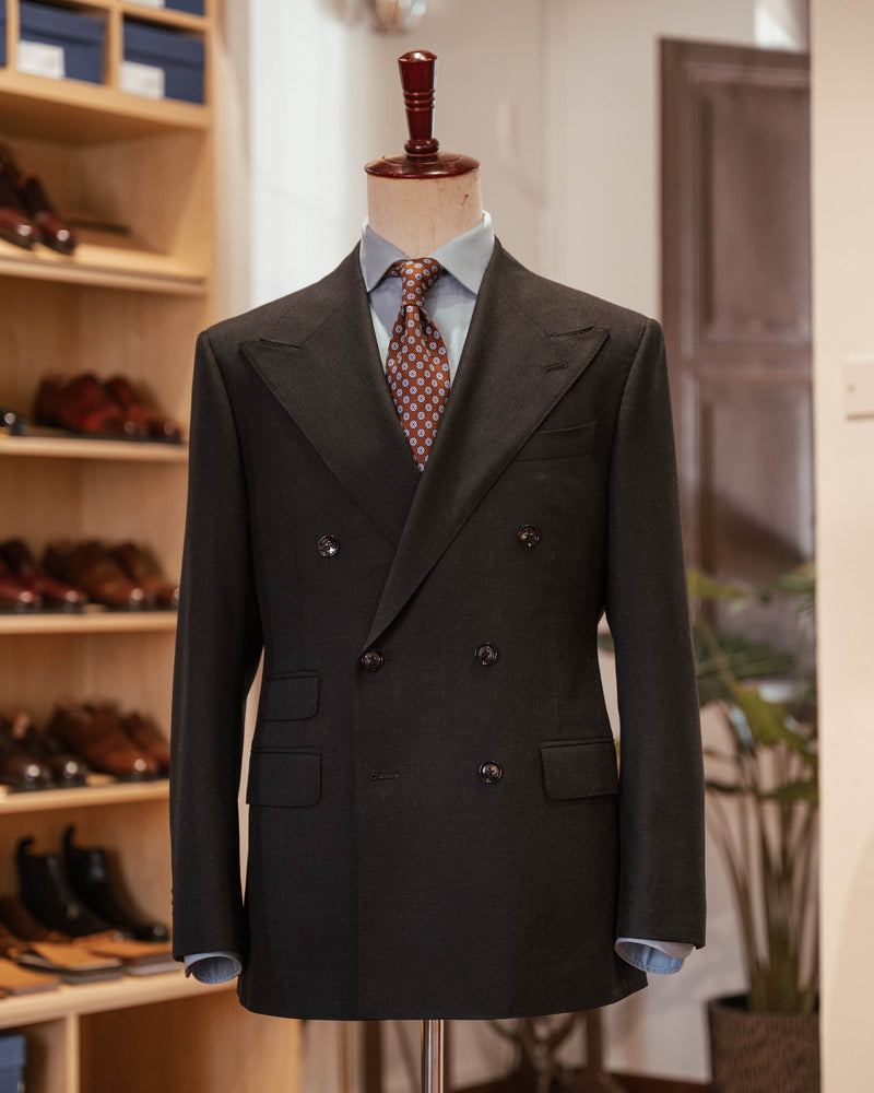 Dark double-breasted suit on a mannequin with a shoe rack in the background