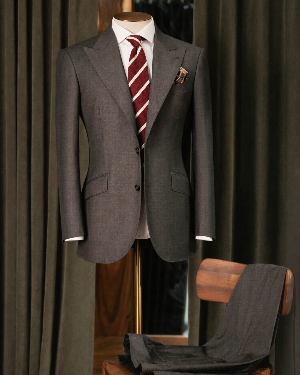 Gray suit with a red tie on a mannequin against a dark curtain background.