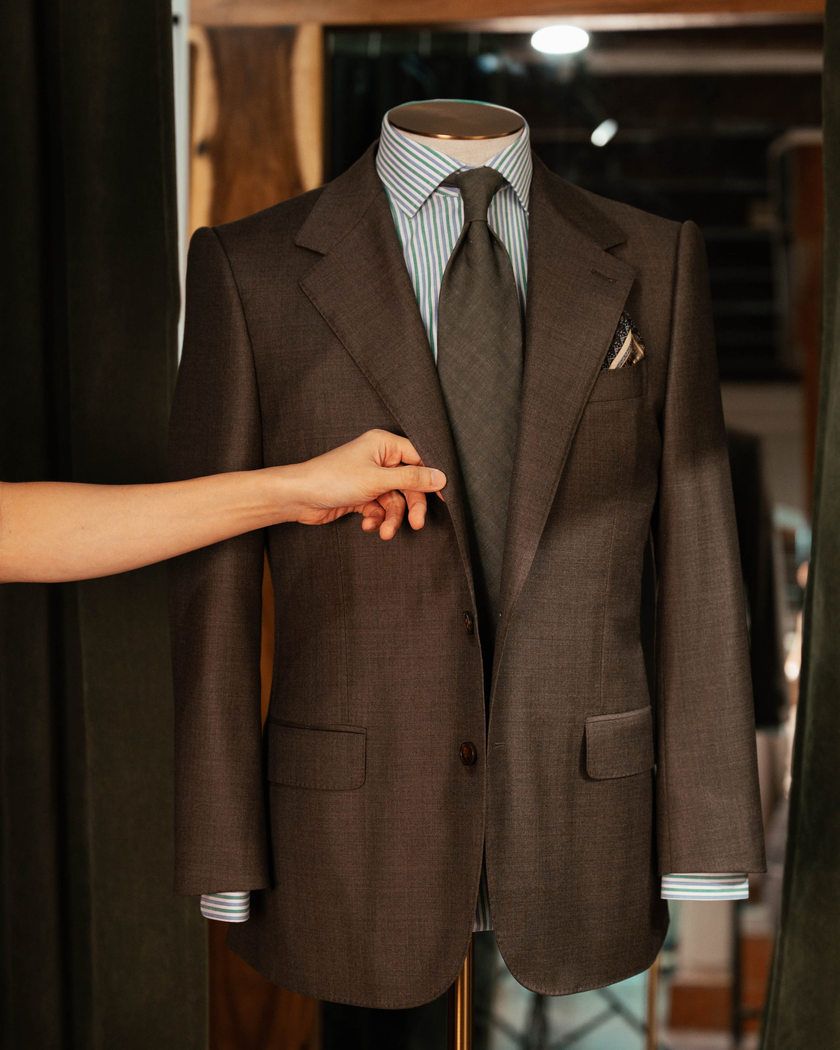 Brown suit jacket on a mannequin with a striped shirt and tie.