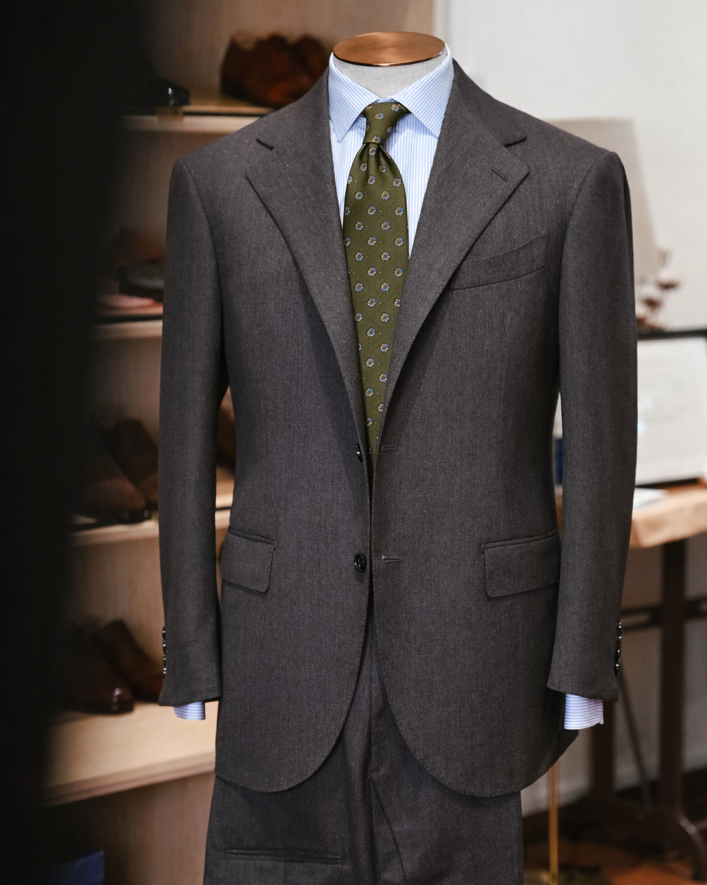 Gray suit jacket with a green tie on a mannequin against a blurred indoor background