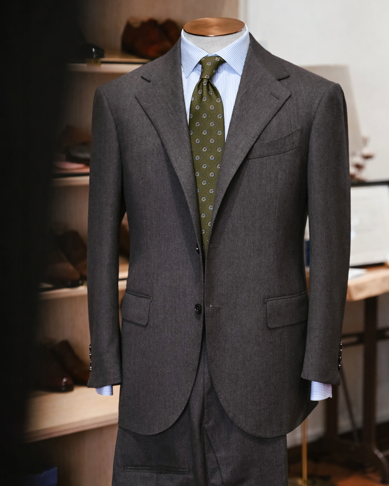 Gray suit jacket with a green tie on a mannequin against a blurred indoor background