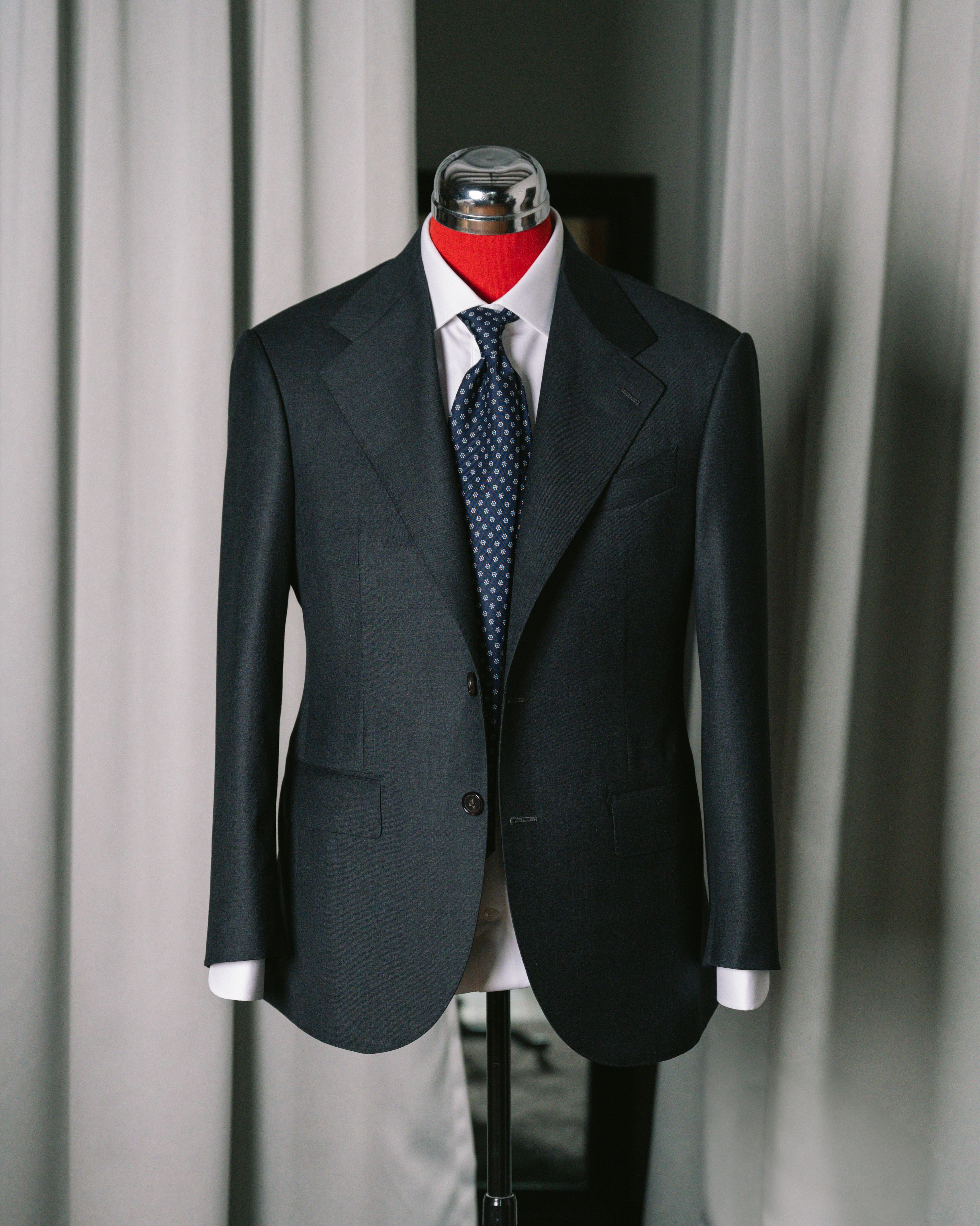 Dark suit with a white shirt and patterned tie on a mannequin against a neutral background