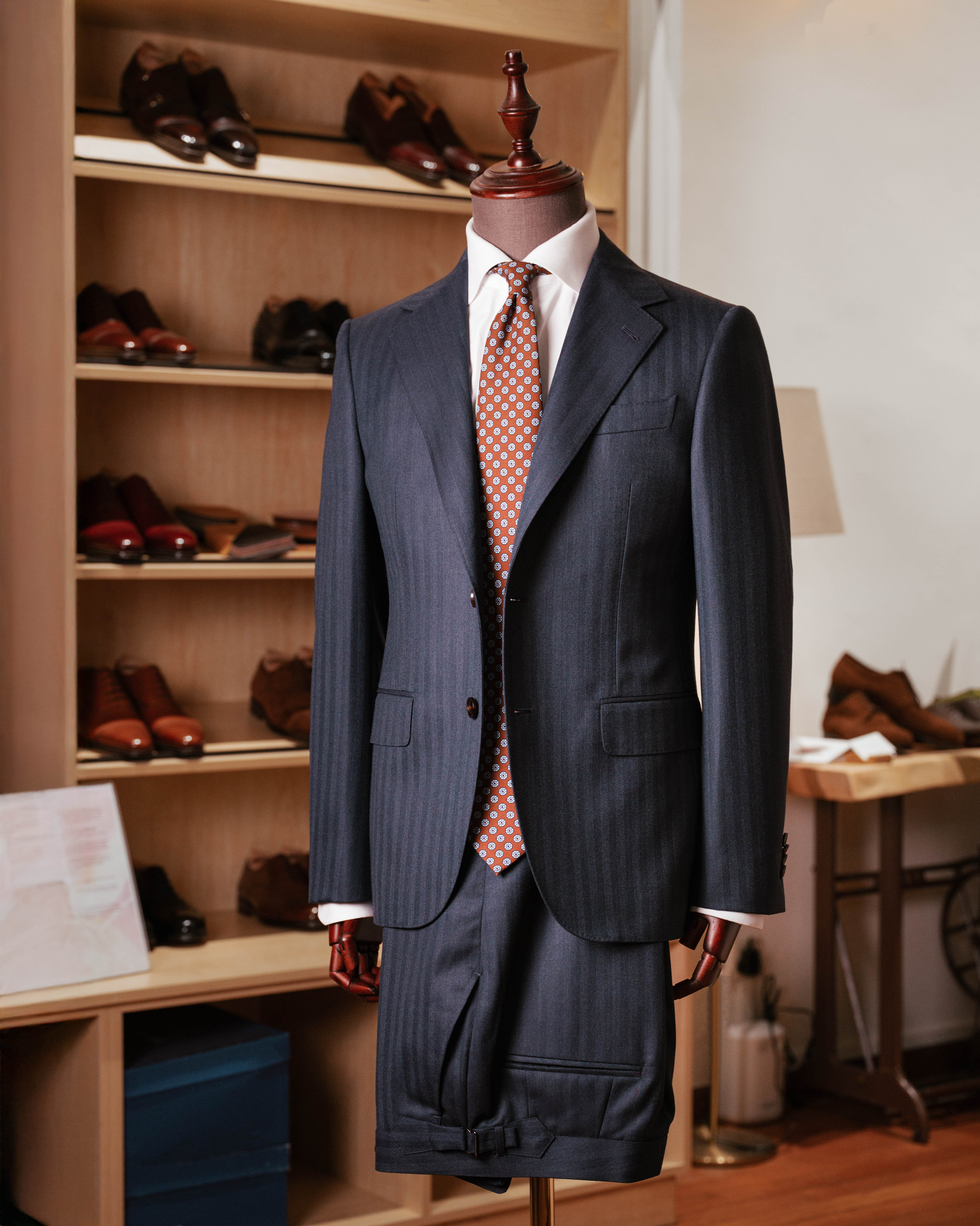 Dark suit with a red patterned tie on a mannequin in a room with shelves of shoes.